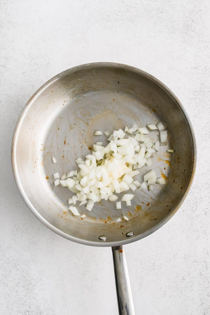 Large stainless steel skillet filled with diced onion.