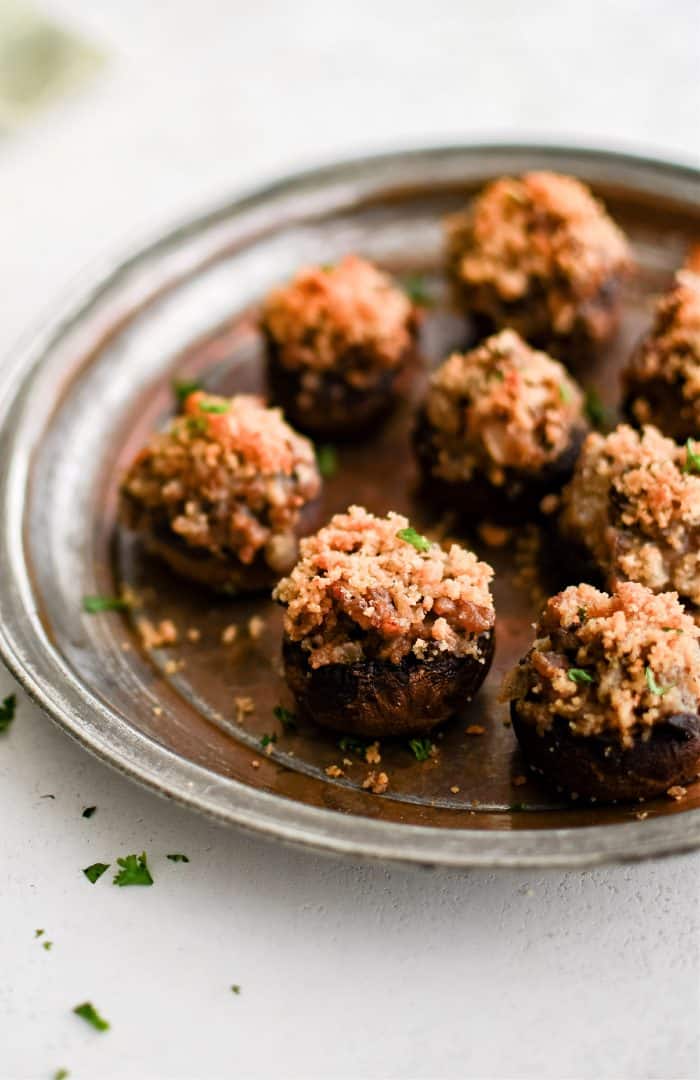 Image of sausage stuffed mushrooms on a silver serving platter topped with crispy golden buttery breadcrumbs and garnished with fresh chopped parsley.