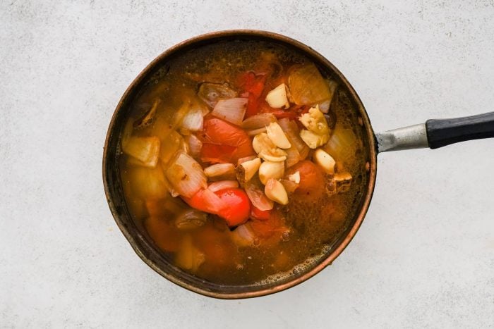 Large soup pot filled with roasted tomatoes, garlic, onion, and red bell pepper with broth.