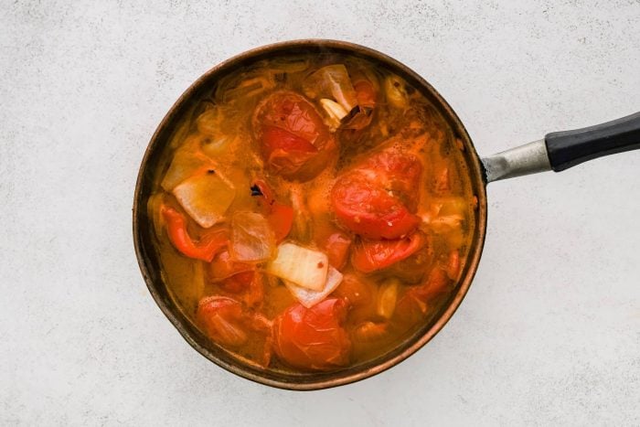 Large soup pot filled with simmering roasted tomatoes, garlic, onion, and red bell pepper with broth.