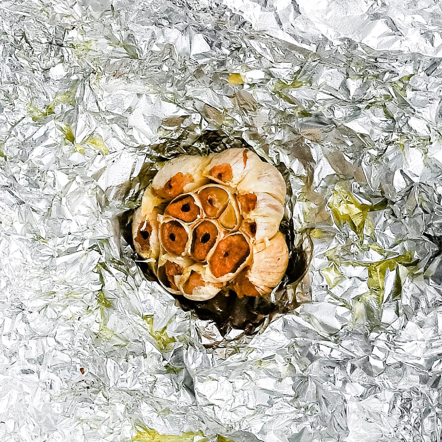 Whole bulb of roasted garlic with golden caramelized cloves on foil.