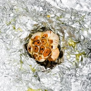 Whole bulb of roasted garlic with golden caramelized cloves on foil.