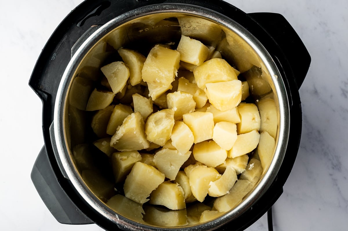 Tender, peeled russet potato chunks with softened edges and slightly broken surfaces fill the stainless steel insert of an Instant Pot after cooking.