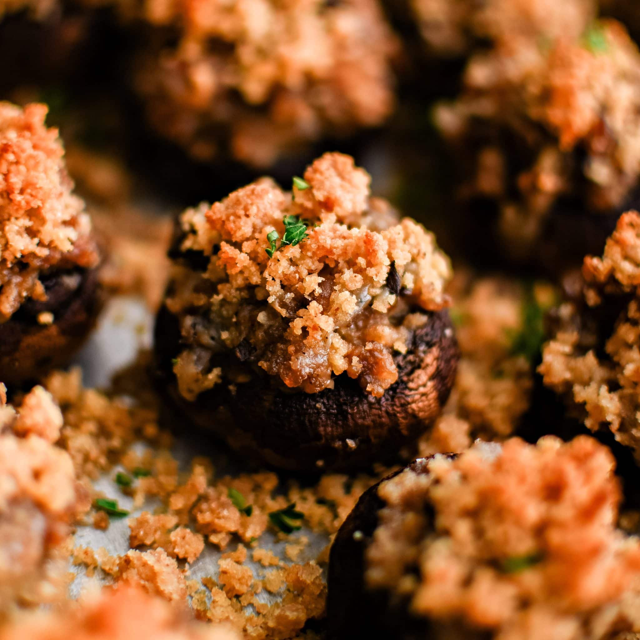 Close up image of sausage stuffed mushrooms on a baking sheet topped with crispy golden buttery breadcrumbs and garnished with fresh chopped parsley.