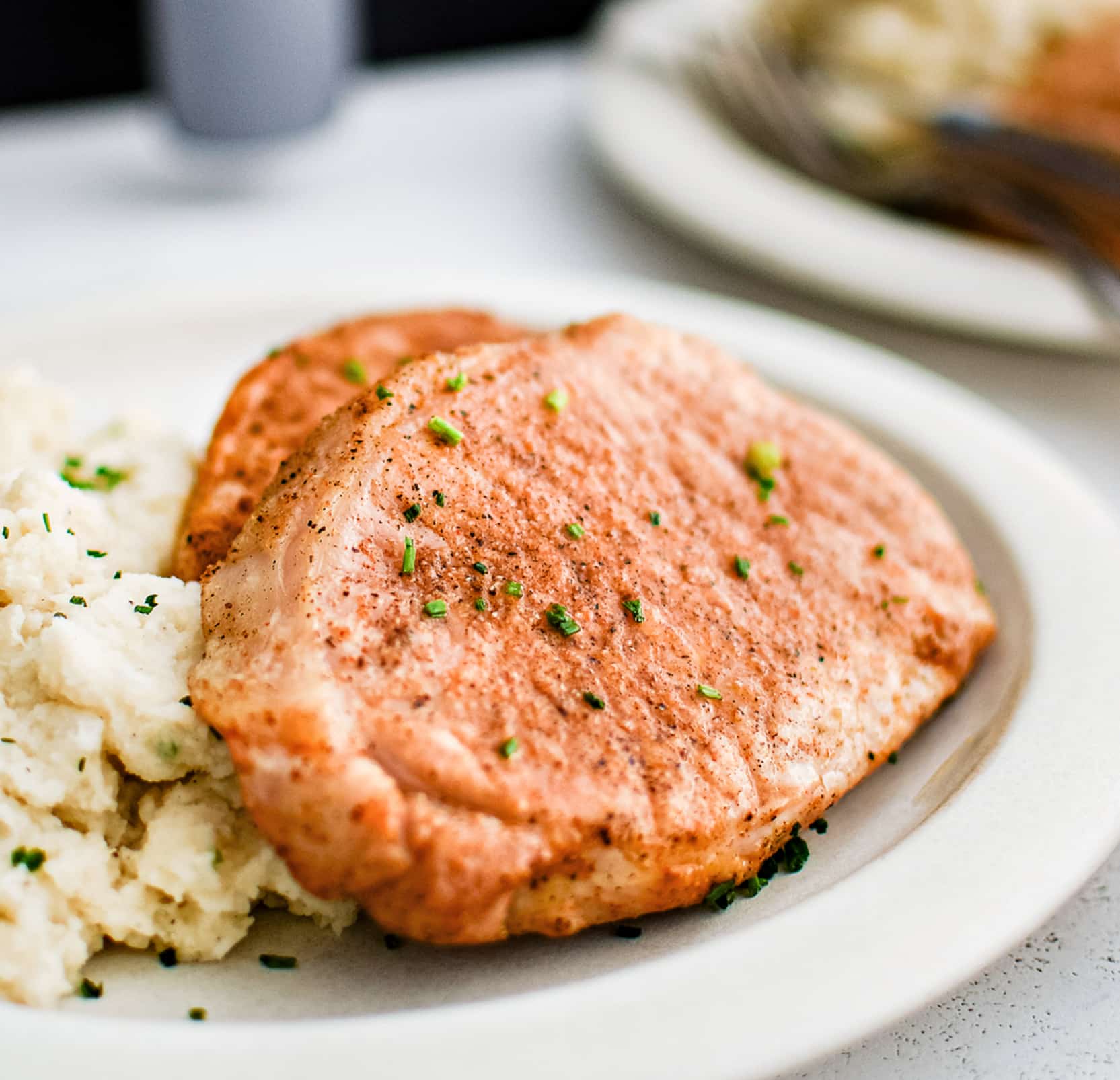 Two boneless cooked pork chops seasoned with paprika, salt, pepper, onion powder, and garlic powder, on a white plate with mashed potatoes.