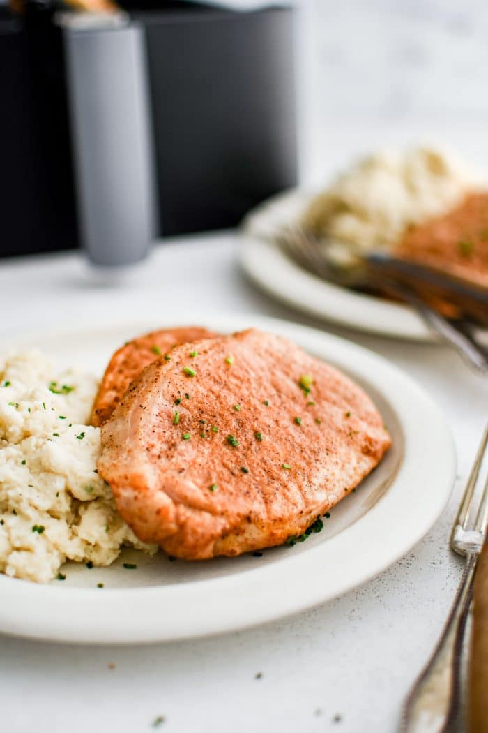 Two boneless cooked pork chops seasoned with paprika, salt, pepper, onion powder, and garlic powder, on a white plate with mashed potatoes.