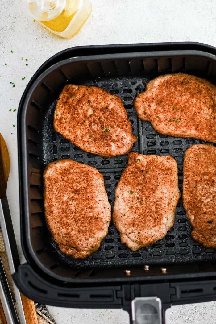 Five boneless cooked pork chops seasoned with paprika, salt, pepper, onion powder, and garlic powder, in the basket of an air fryer.