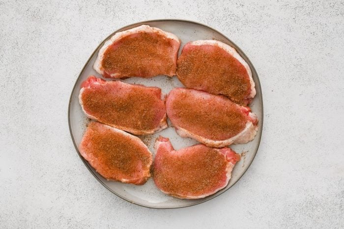 Six seasoned boneless pork chops on a white plate.