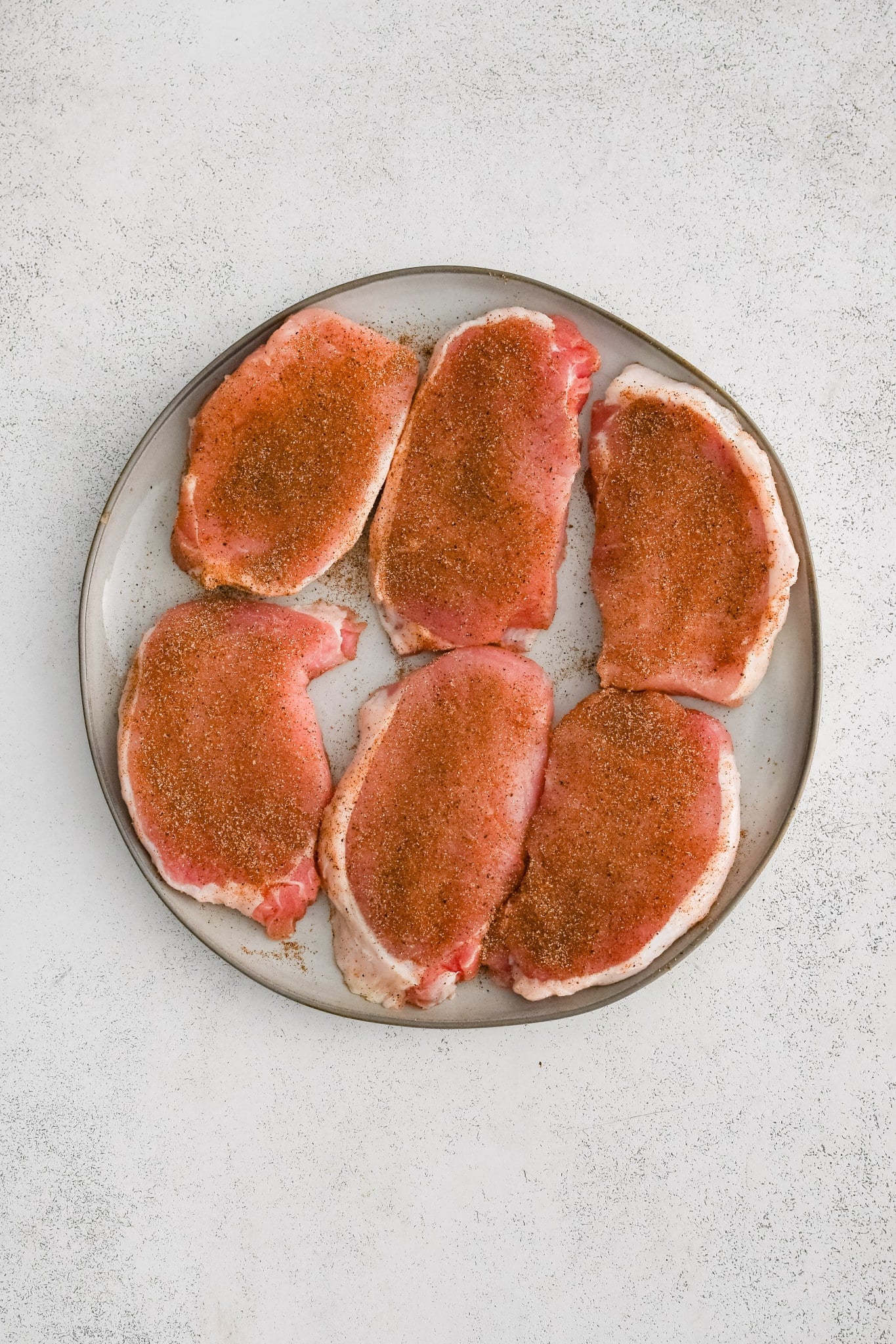Six seasoned boneless pork chops on a white plate.