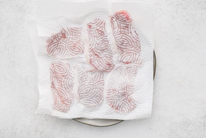 Patting dry six raw boneless pork chops on a white plate.