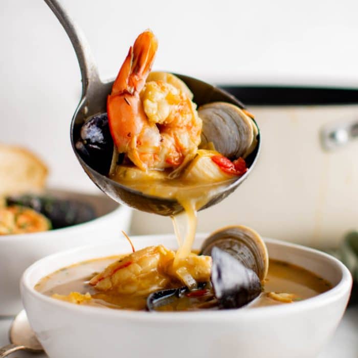 Large ladle filled with French Bouillabaisse made with shrimp, mussels, and clams in a rich broth.