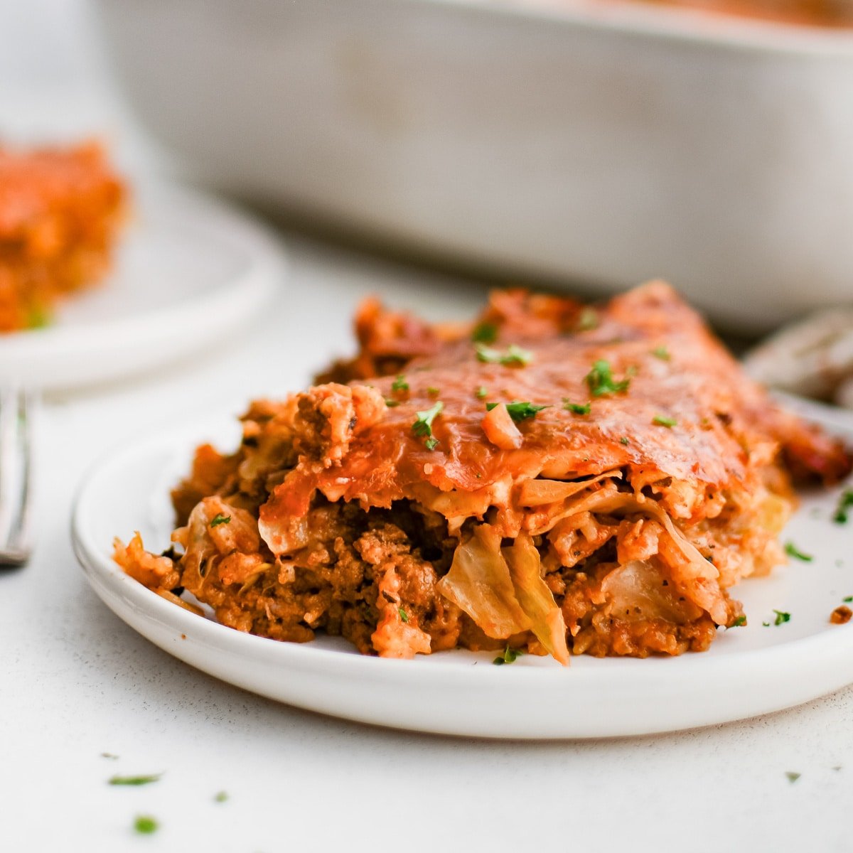 Serving of cabbage roll casserole made with green cabbage, rice, and ground beef in a comforting tomato sauce on a white plate.