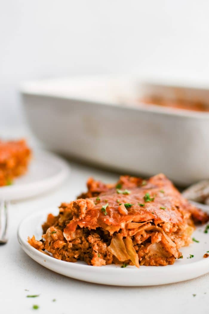 Serving of cabbage roll casserole made with green cabbage, rice, and ground beef in a comforting tomato sauce on a white plate.