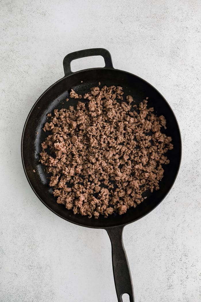 Large cast iron skillet filled with one pound of cooked lean ground beef.