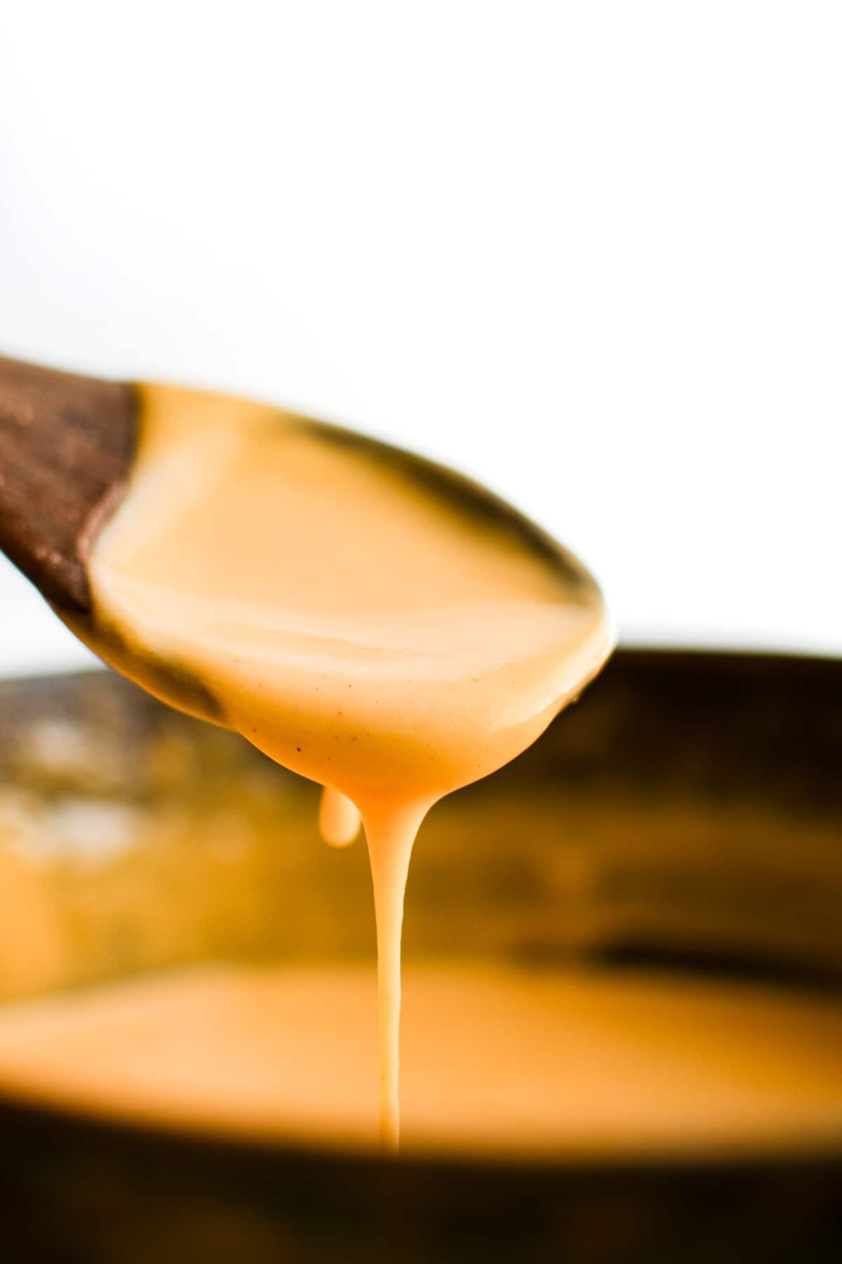 Wooden spoon filled with drippy, silky smooth, and creamy cheese sauce made from all-natural ingredients.