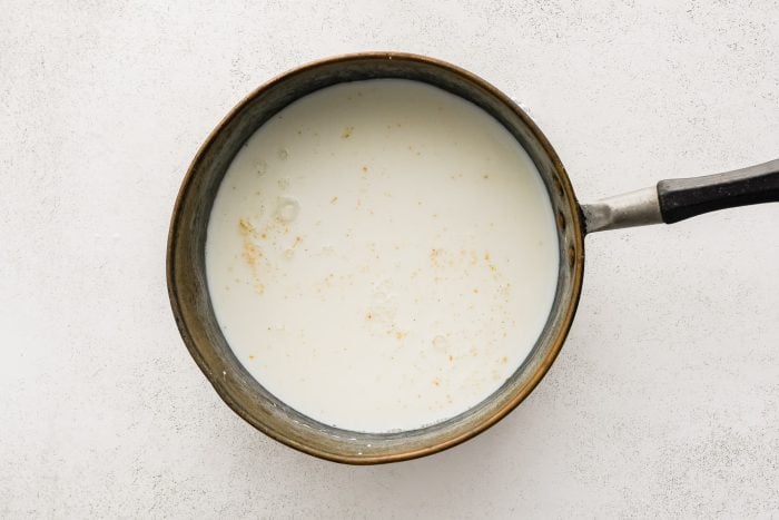 Whole milk added to a medium pot filled with seasoned white roux.