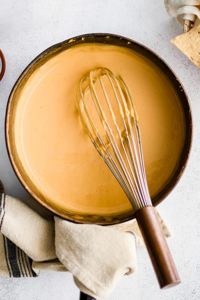 Whisk resting in a medium sauce pot filled with silky smooth cheese sauce made from all-natural ingredients.