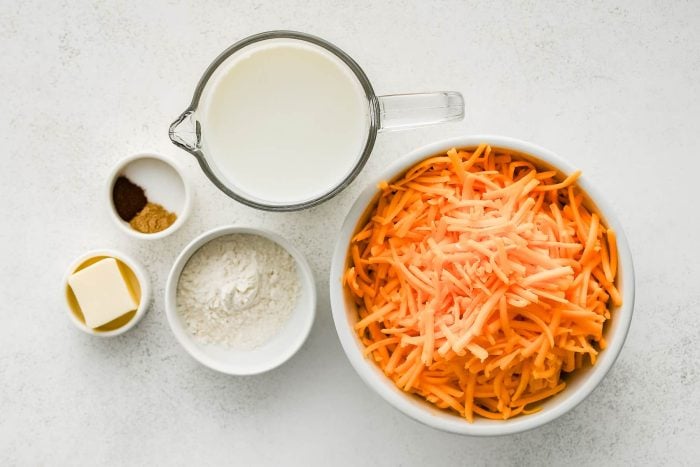 All of the ingredients needed to make cheese sauce in individual bowls, measuring cups, and ramekins.