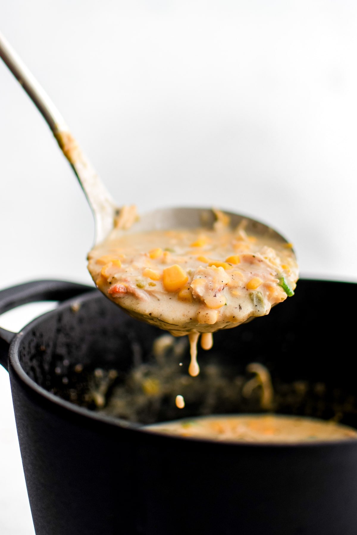 Large soup ladle over a large cast iron pot filled with creamy corn and chicken chowder.