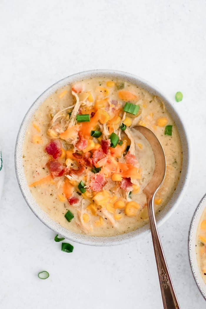 White soup bowls filled with corn and chicken chowder and garnished with shredded cheddar cheese, crispy bacon, and green onions.