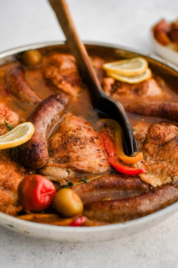 Large pan filled with prepared chicken scarpariello filled with crispy braised chicken thighs and Italian sausage in a rich broth with onions and bell peppers.