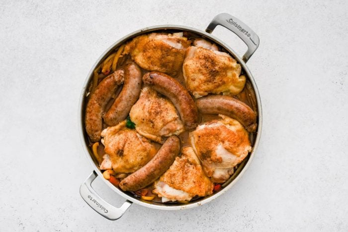 Seared chicken thighs and browned Italian sausage set on top of sliced bell peppers and onions in a rich broth.