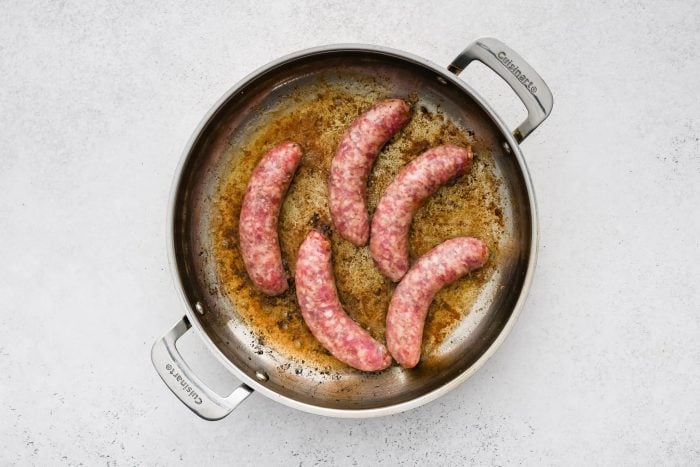 Five large raw Italian sausages in a large skillet.