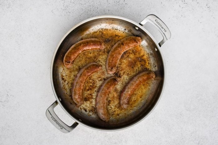 Five large Italian sausages browning in a large skillet.