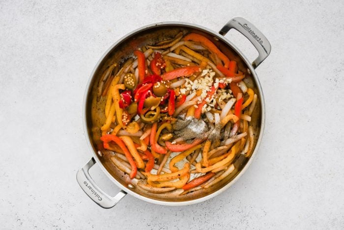 Jarred cherry peppers and fresh garlic added to a large skillet filled with softened bell peppers and onion.