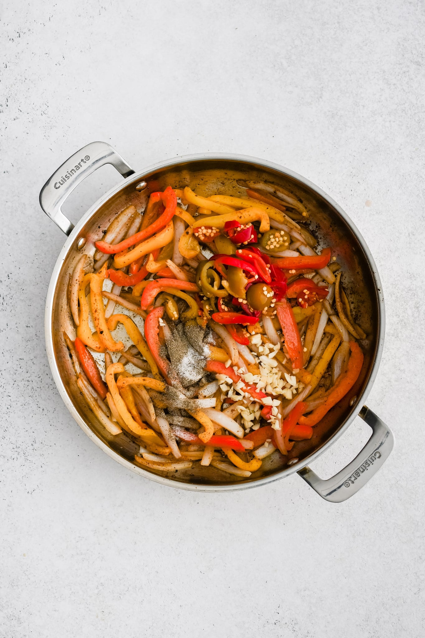 Jarred cherry peppers and fresh garlic added to a large skillet filled with softened bell peppers and onion.