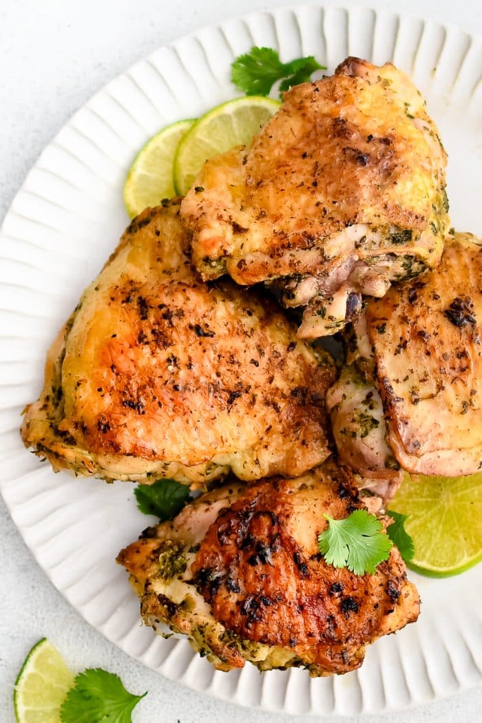 Large white serving plate topped with four juicy cooked chicken thighs marinated in cilantro lime marinade.