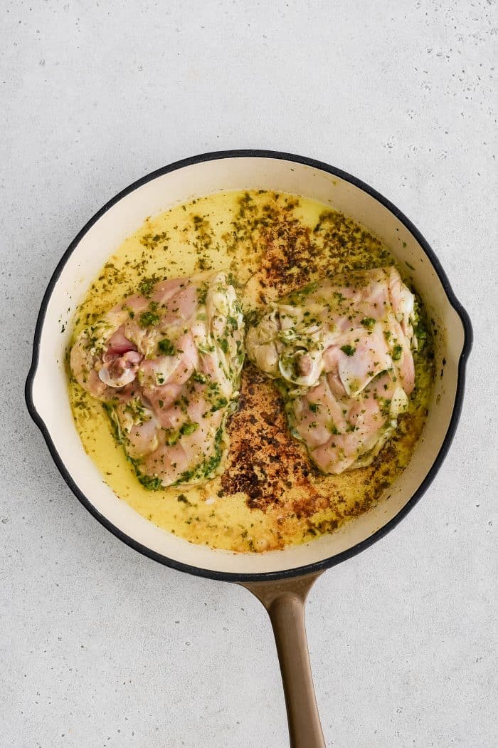 Large oven-safe skillet with two marinated chicken thighs skin-side-down.