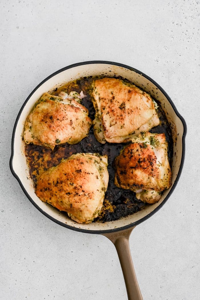 Large oven-safe skillet with four marinated and golden baked chicken thighs.