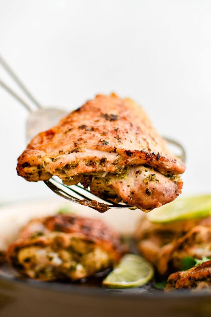 Metal spatula balancing a juicy cooked chicken thigh marinated in cilantro lime marinade.