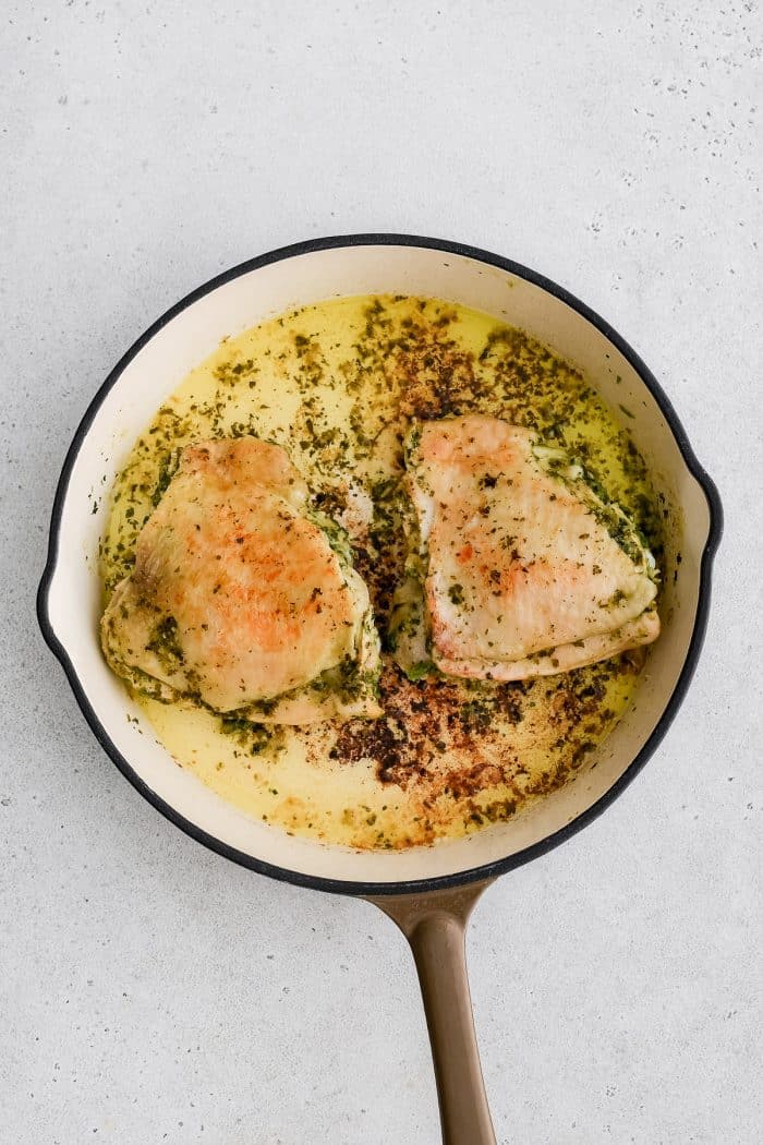 Two cilantro lime marinated chicken thighs searing in a large oven-safe skillet.