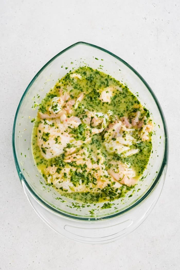 Large glass mixing bowl filled with chicken thighs in homemade cilantro lime marinade.