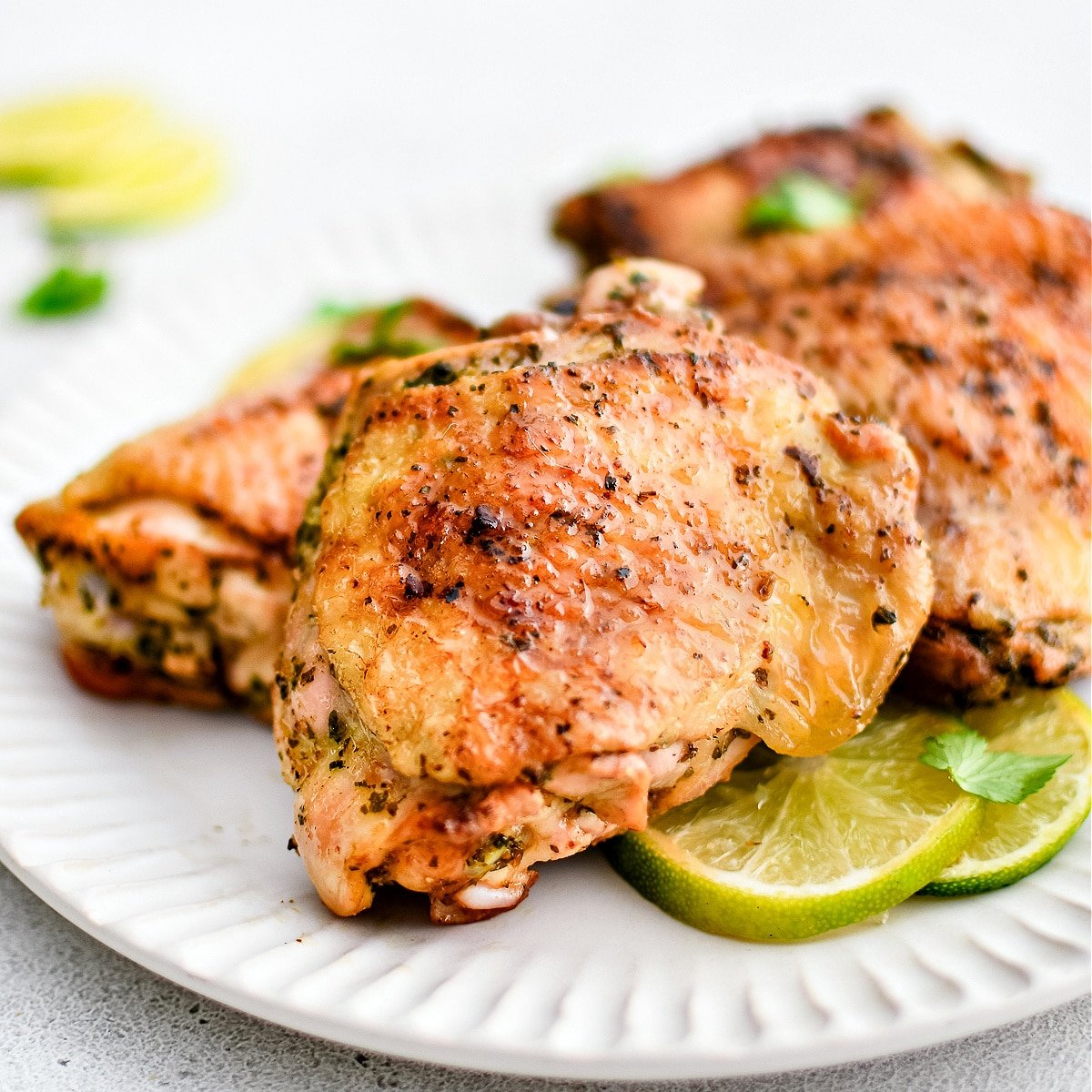 Large white serving plate topped with four juicy cooked chicken thighs marinated in cilantro lime marinade and served with fresh lime slices.