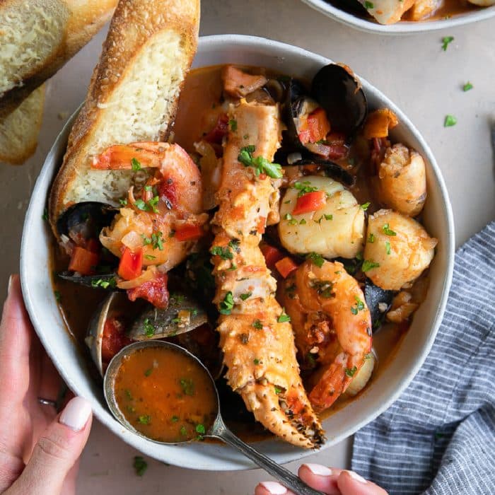 White soup bowl filled with an assortment of seafood in a tomato-based broth.