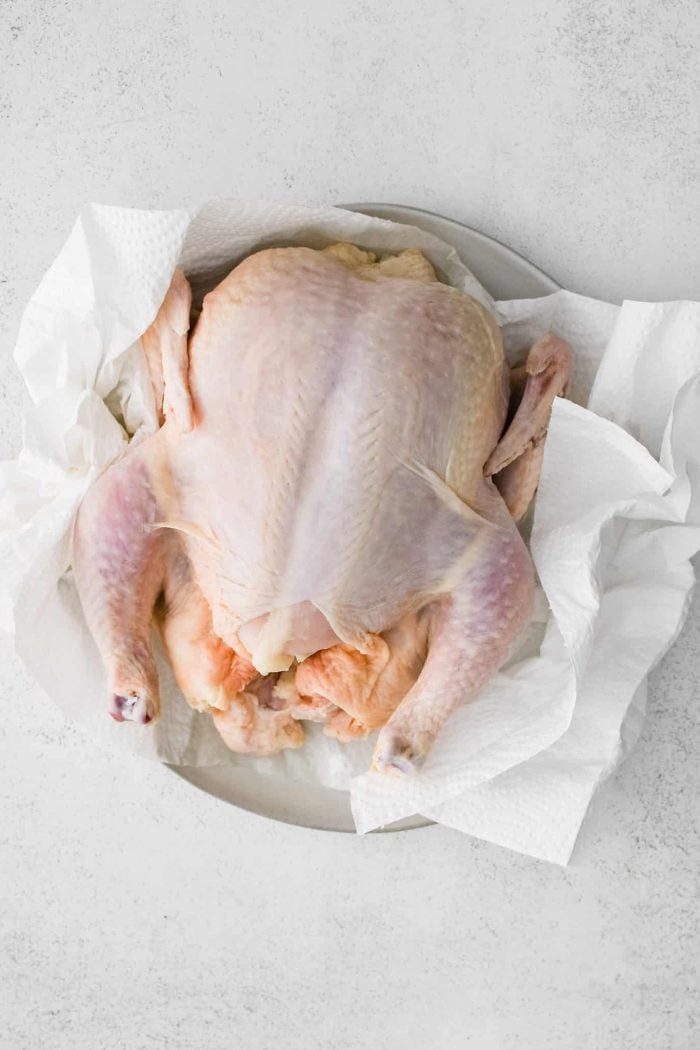 Raw, uncooked whole chicken on a plate lined with paper towels.