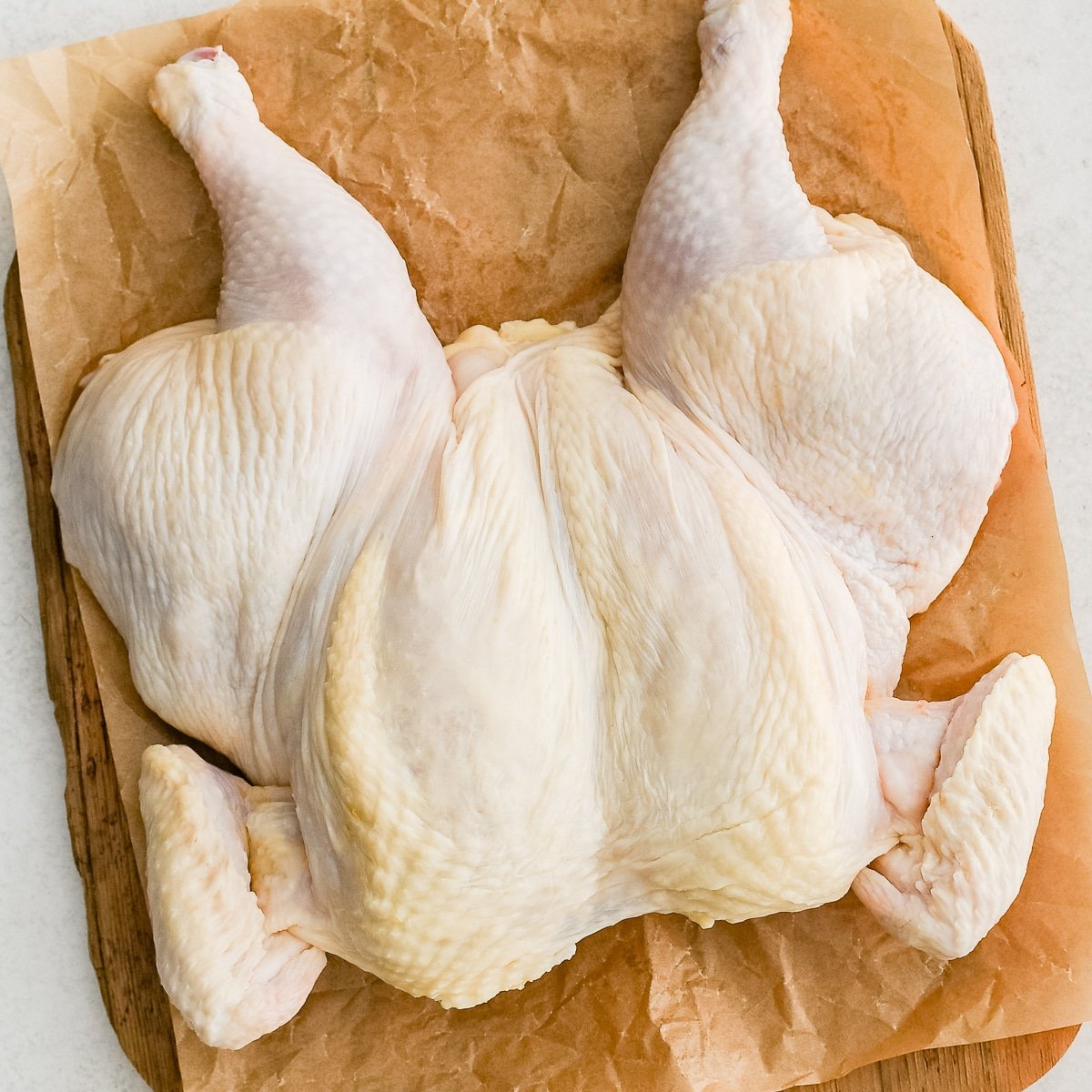 A raw, uncooked spatchcock chicken on a large cutting board flattened with breast-side-up.