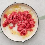 Large skillet with softened white onion and raw ground beef.