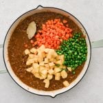 Diced potatoes, carrots, and peas added to a large skillet filled with simmering ground beef in homemade tomato sauce.