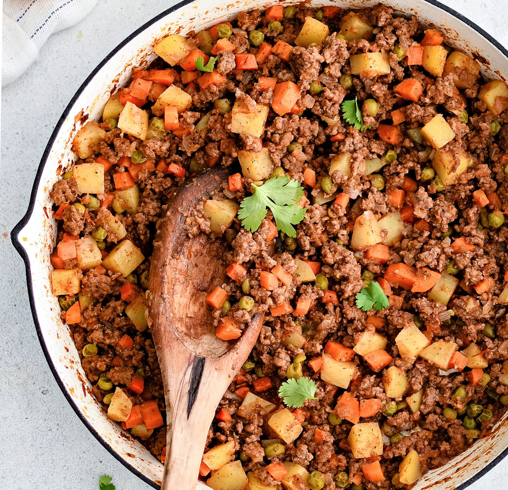 Large pan filled with Mexican style picadillo with ground beef, potato, carrots, and peas, in a seasoned tomato sauce.