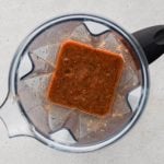 Blender filled with pureed garlic cloves, jalapeno, tomatoes, whole pieces of onion, oregano, beef bouillon, salt, pepper, ground cumin, and two cups of water.