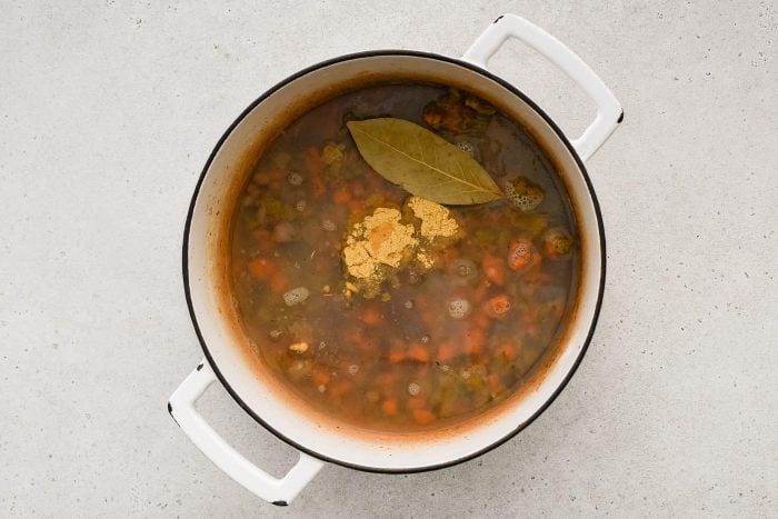 Water, clam juice, bouillon powder, Worcestershire sauce, and bay leaf added to a large pot filled with softened onion, carrots, and celery coated in roux.