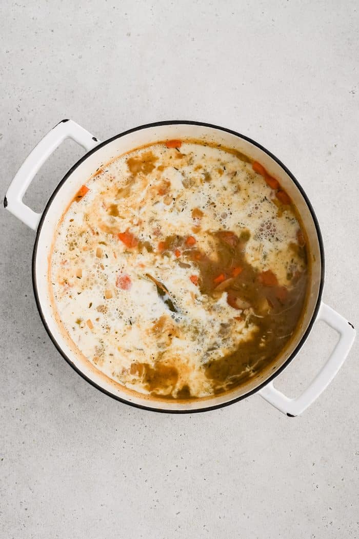 Half-and-half added to a large Dutch oven filled with simmering potatoes, onion, carrots, and celery.