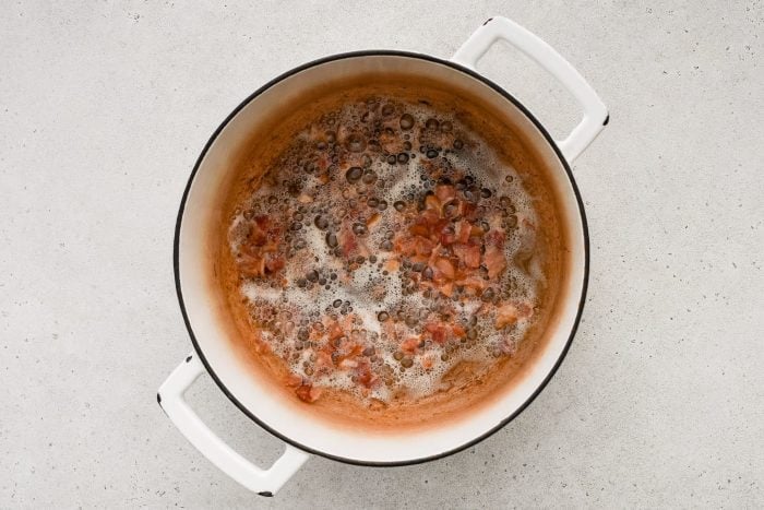 Chopped bacon cooking in a large white Dutch oven.