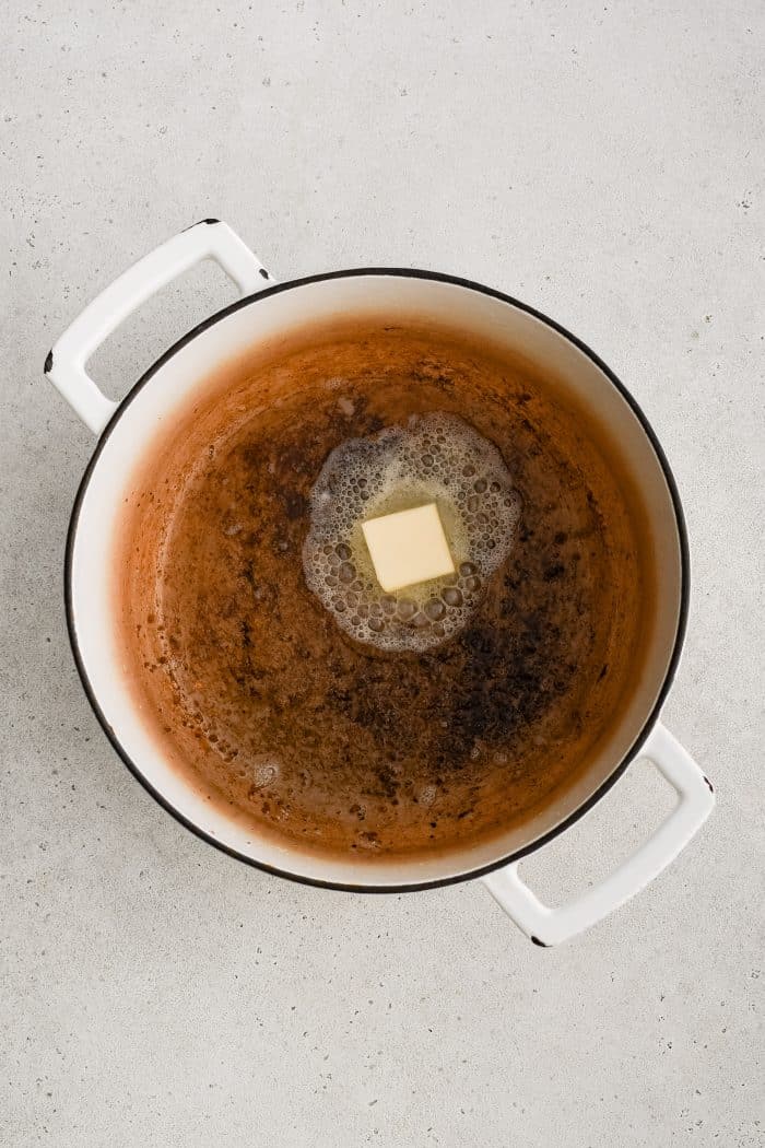 Butter melting in a large white Dutch oven filled with two tablespoons of rendered pork fat.