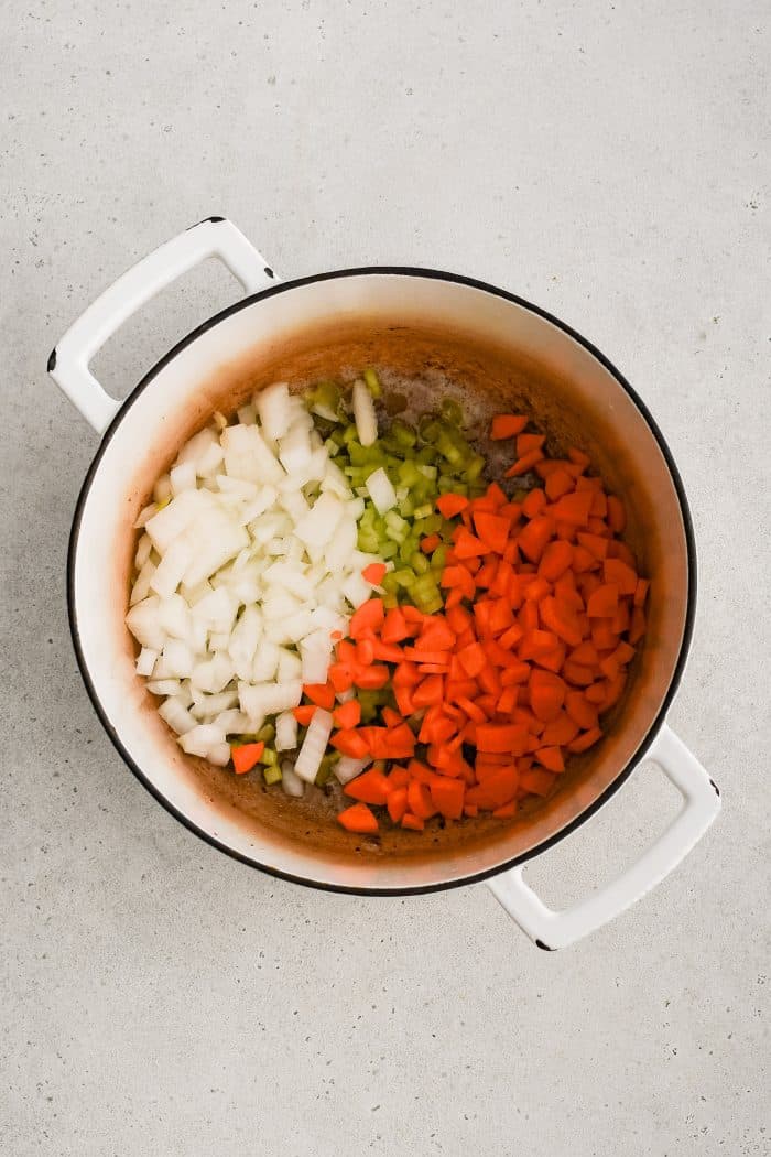 Chopped onion, celery, and carrots added to a large white Dutch oven.