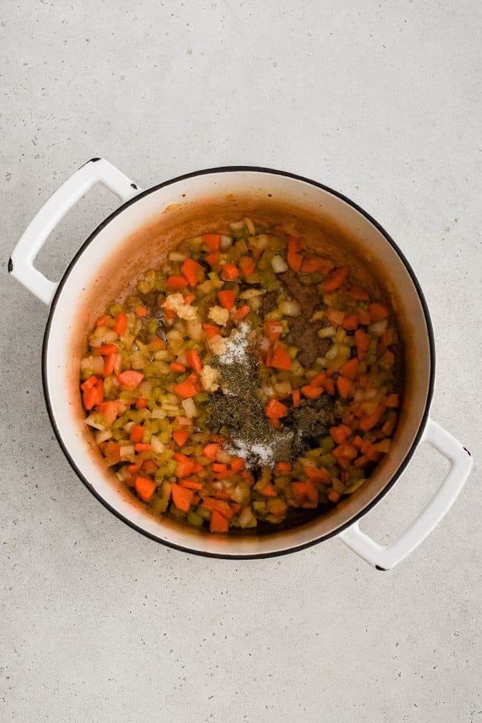 Garlic, thyme, pepper, and salt added to onion, celery, and carrots cooking slowly in butter and rendered bacon fat in a large white Dutch oven.